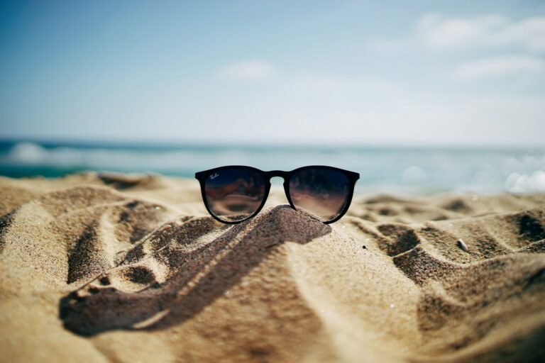 Sunglasses on sandy beach near ocean symbolizing summer travel tips for hot weather